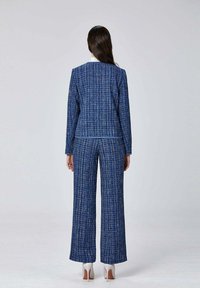 Costume en tweed bleu avec une veste structurée et un pantalon à jambes larges, présentant un motif texturé et des accents blancs, vu de dos.