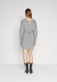 Abito grigio lavorato a maglia con maniche lunghe, vita aderente e schiena scoperta legata con un nastro, abbinato a stivali da cowboy neri con intricati motivi bianchi.