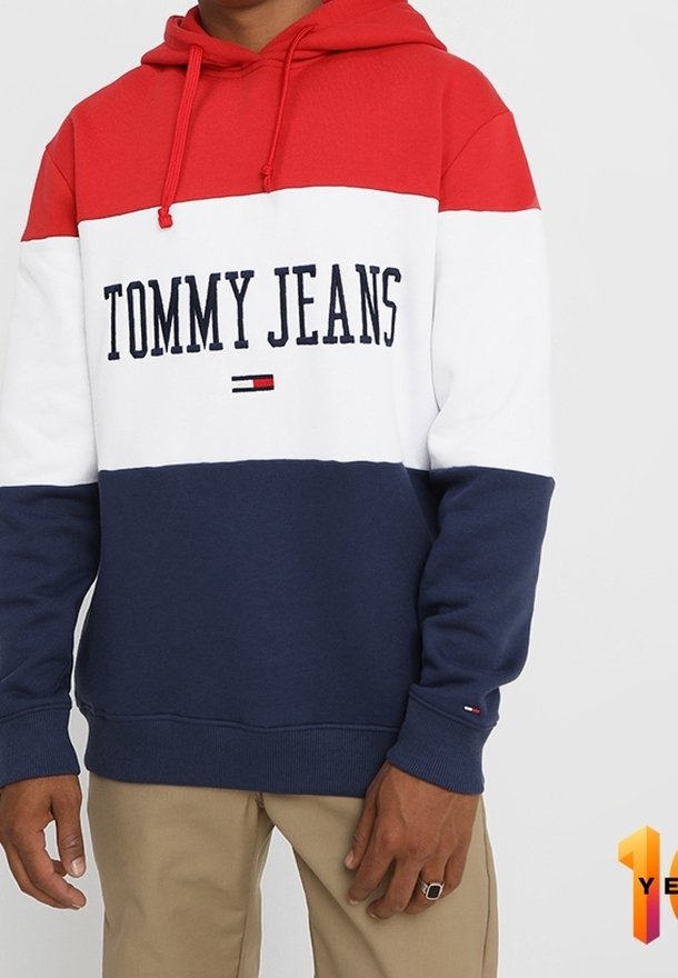 Felpa con cappuccio a blocchi di colore rosso, bianco e blu navy realizzata in tessuto morbido. Presenta una tasca a marsupio, un cappuccio regolabile con coulisse e il logo "TOMMY JEANS".