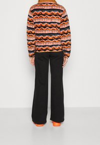 Kolorowy, wzorzysty sweter w kolorach pomarańczowym, różowym i czarnym z okrągłym dekoltem, zestawiony z czarnymi szerokimi spodniami i pomarańczowymi butami na platformie.
