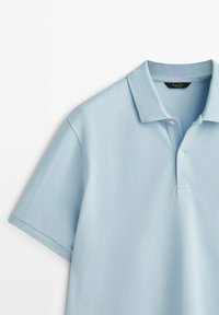 Lichtblauw polohemd met korte mouwen, kraag en twee witte knopen, plat liggend op een witte achtergrond.
