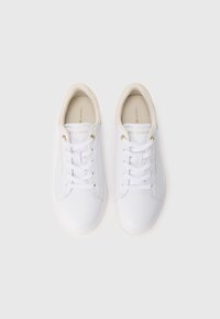 Hvite lave joggesko med beige innerfôr, hvite lisser, gullhull og merkevaretekst på tunga og sidene, vist ovenfra.