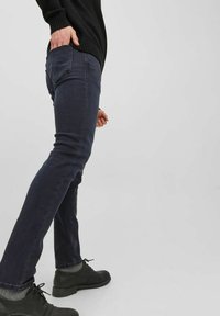 Mörkblå slim-fit jeans med en slät textur, med en femficksdesign och subtila sömnadsdetaljer, kombinerat med svarta snörskor.