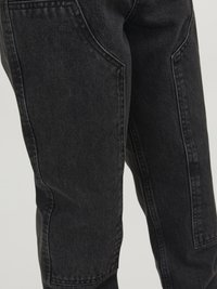 Svarta denimbyxor med en avsmalnande design, synliga sidofickor och en strukturerad tyg. Sömmarna är kontrasterande, vilket framhäver kanterna.