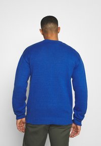 Niebieski sweter z dzianiny z prążkowymi mankietami i dolnym neu, charakteryzujący się luźnym krojem i teksturowanym materiałem, widoczny z tyłu.