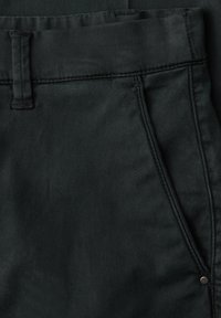 Primo piano di pantaloni in tessuto nero che mostrano la cintura, il passante per la cintura, la tasca laterale e il dettaglio del rivetto.