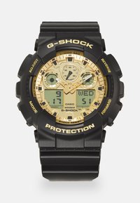 Montre numérique-analogique noire avec des accents dorés, grand cadran rond, bracelet en caoutchouc, trois sous-cadrans et marque "G-SHOCK". Étanche, résistant aux chocs.