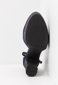 Élégante chaussure à talon haut bleu marine avec une semelle noire texturée et un talon argenté scintillant. Présente un design épuré et une bride à la cheville.