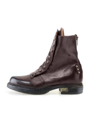 Bottine en cuir marron foncé avec rabat déboutonné montrant des œillets métalliques et un talon bas empilé avec une petite plaque métallique sur le côté extérieur.
