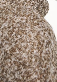 Tessuto marrone con una texture morbida e pelosa. Il materiale presenta un mix di fili chiari e scuri, creando un aspetto caldo e stratificato.