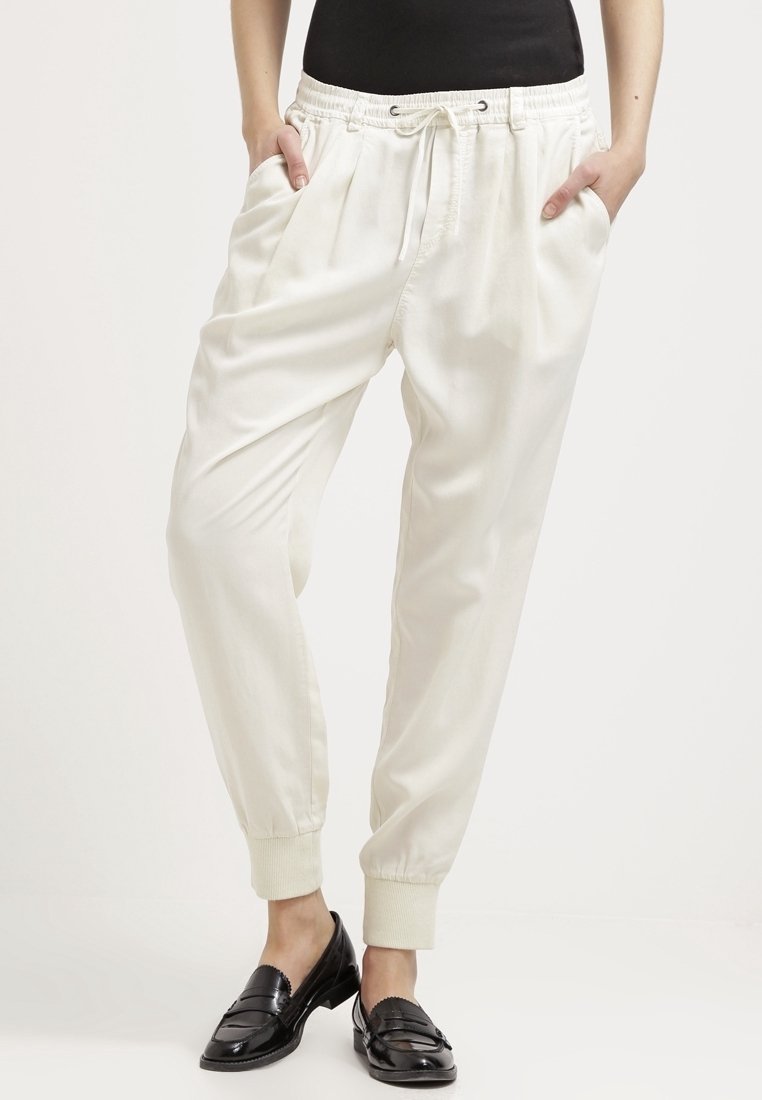 Pantalons blancs amples avec une taille élastique et un cordon de serrage, dotés de poches latérales et de poignets fuselés. Texture lisse et matériau léger.