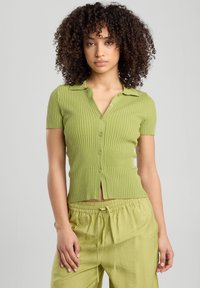 Short-sleeve, ribbed knit button-up top in light green, featuring a collar and a front slit, paired with loose matching pants.