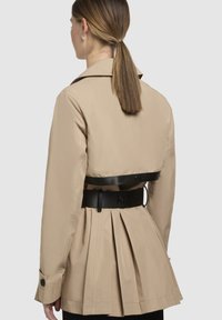 Khaki trenchcoat met een aangesloten ontwerp, zwarte riem, geplooide achterkant en knoopmanchetten, met een zachte textuur en een op maat gemaakte afwerking.