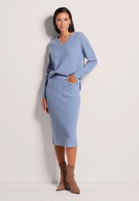 Helles blaues geripptes Strickpullover mit V-Ausschnitt und langen Ärmeln, kombiniert mit einem passenden rocklangen Rock mit Seitentaschen. Braune Knöchelstiefel.