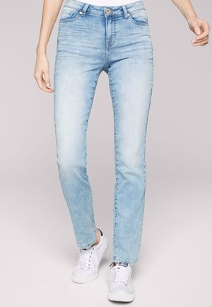 Helle Jeans aus Denim, mit schmalem Schnitt, fünf Taschen und Knopfverschluss, kombiniert mit weißen Sneakern.