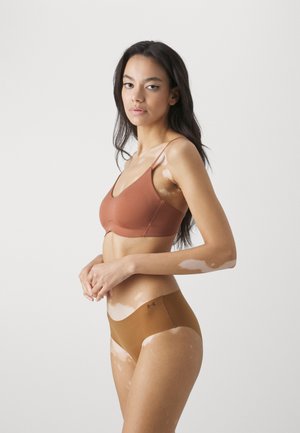 Smeđi bralette s tankim trakama i bešavnim dizajnom uparen s odgovarajućim smeškim gaćicama, koje imaju suptilnu oznaku na elastiku.