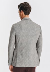 Szary wełniany żakiet o dopasowanym kroju, z klapami typu notch i subtelną teksturą. Posiada pojedynczy rozcięcie z tyłu oraz zapięcia na guzikach przy mankietach.