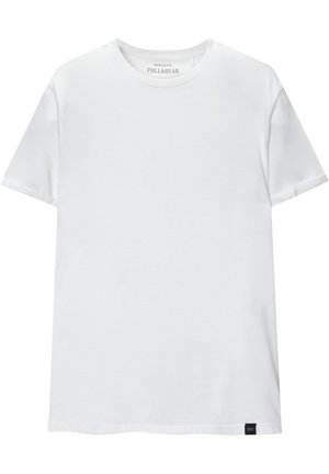 Weißes Muskel-fitt T-Shirt aus Baumwolle. Rundhals, kurze Ärmel, glatte Textur. Kleines schwarzes Logo-Tag am Saum. Schlichtes Design.