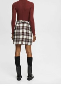 Top de manga larga burdeos combinado con una falda corta de cuadros en blanco, negro y marrón. La modelo lleva botas negras hasta la rodilla con suelas texturizadas.