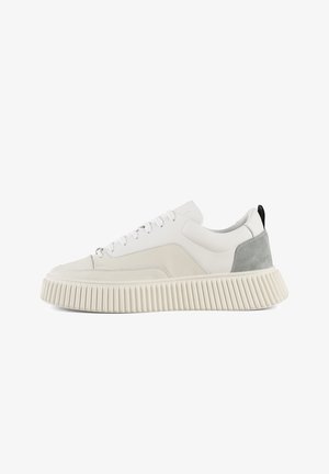 Sneaker bianco con tomaia in pelle liscia, tallone in suede grigio, suola in gomma crema con texture e stringhe bianche. Design della suola con righe audaci.