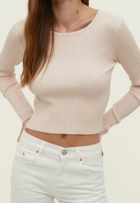 Helles rosa, geripptes Langarmoberteil mit rundem Ausschnitt, figurbetontem Schnitt und strukturiertem Stoff, kombiniert mit weißen, hochgeschnittenen Jeans.