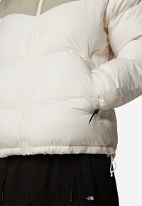 Puffjacka i off-white med olivgrön accent vid bröstet, med en framtida dragkedja, kviltad struktur och justerbar nederdel.