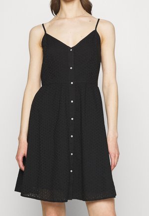 Vestido negro sin mangas con un cuerpo ajustado, falda en línea A, tejido texturizado y botones blancos que bajan por la parte delantera.