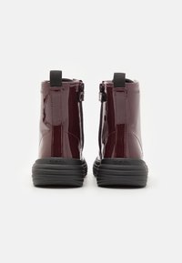 Burgundy patent leather ankle boots with a black rubber sole, featuring a side zipper and pull tab for easy wear.
