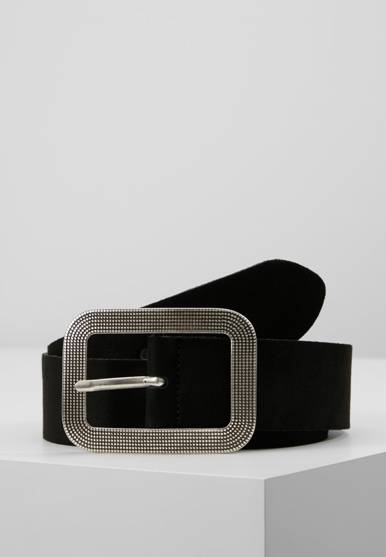 Ceinture en daim noire avec une grande boucle rectangulaire argentée texturée reposant sur une surface d'angle blanche.