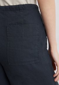 Donker marineblauwe linnen broek met een gestructureerd oppervlak, voorzien van een patchzak op de achterzijde. De tailleband is elastisch voor extra comfort.