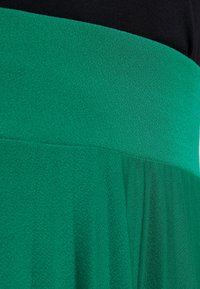 Abito lavorato a maglia con corpino nero e gonna verde dal finish texture. La gonna presenta leggeri arricciamenti vicino alla vita.