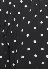 Tessuto nero con un design fluido caratterizzato da pois bianchi. La texture appare liscia con accenti arricciati che ne aumentano il dettaglio visivo.