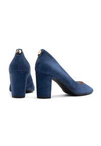 Chaussures à talons hauts en daim bleu marine, avec un bout carré, un talon épais et un bouton doré sur l'arrière. Texture lisse, design épuré.