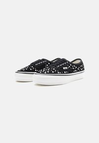 Adidași din suede negru cu puncte albe, șireturi negre și o talpă din cauciuc alb. Au o dungă contrastantă neagră de-a lungul marginii tălpii.