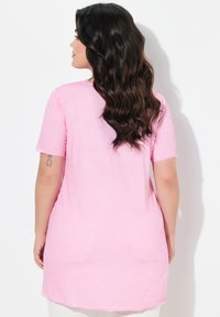 Túnica rosa de manga corta con un corte relajado, dobladillo asimétrico y tejido suave y ligero. Detalles de costura mínimos en las mangas.