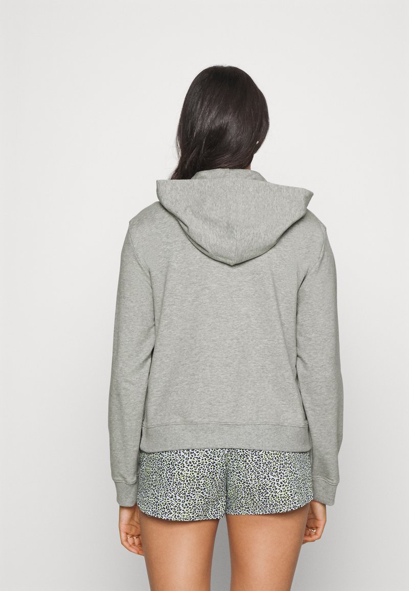Sudadera gris con un corte holgado y una capucha ajustable, fabricada en tela suave. Combinada con pantalones cortos estampados que presentan un diseño de leopardo en verdes y negros.