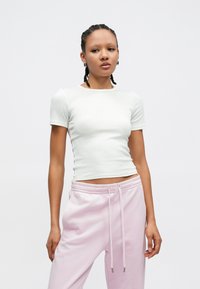 Λευκό ριμπ κομψό τοπ με κοντό μανίκι, συνδυασμένο με ροζ παστέλ φόρμες με ελαστική μέση και κορδόνι. Απλός, εφαρμοστός σχεδιασμός.