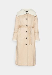 Long manteau beige boutonné avec col et poignets en shearling blanc, taille ceinturée et longueur mi-mollet sur fond uni.