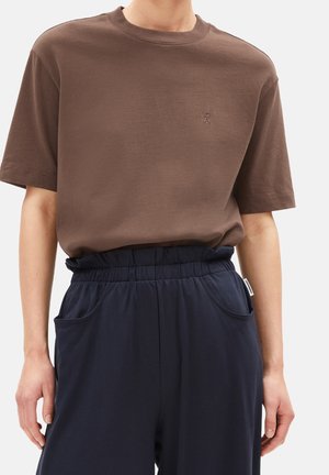 Brun bomuld t-shirt med rund hals og korte ærmer, med en lille tonet logo på brystet. Kombineret med navyblå bukser med elastik i taljen.