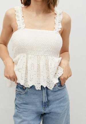 White peplum top with textured smocking, ruffled straps, and embroidered eyelet hem. Paired with light blue denim jeans.