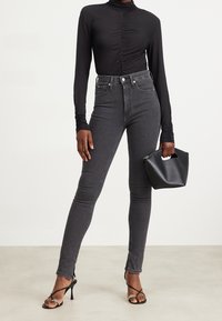 Svart långärmad topp med framrarrangemang, högmidjade grå smala jeans, öppna svarta sandaler med remmar och en liten svart handväska.