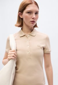 Μπεζ πόλο μπλούζα με κοντά μανίκια και γιακά, με κουμπιά στο μπροστινό μέρος και κεντητό λογότυπο στον τόνο του υφάσματος στο στήθος.