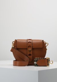 Braune Leder-Crossbody-Tasche mit Klappenverschluss, dekorativem Riemen und goldenen Beschlägen. Verfügt über eine strukturierte Oberfläche und eine abgerundete Form.