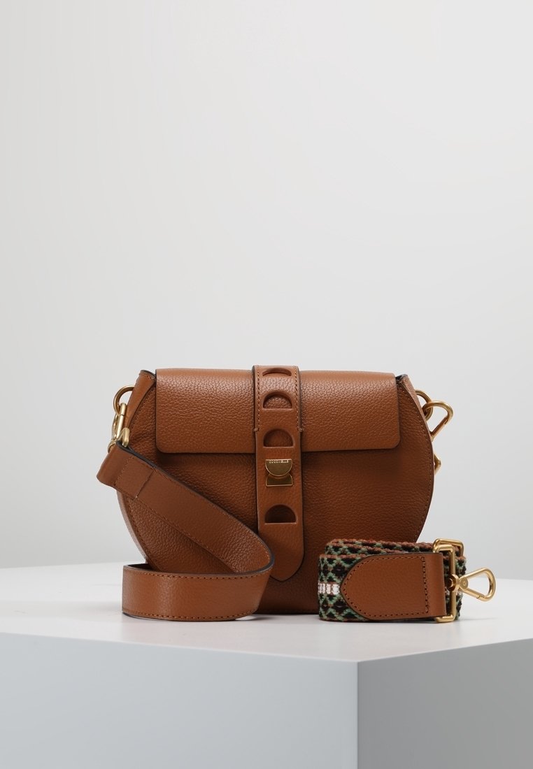 Braune Leder-Crossbody-Tasche mit Klappenverschluss, dekorativem Riemen und goldenen Beschlägen. Verfügt über eine strukturierte Oberfläche und eine abgerundete Form.