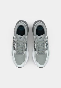 Szare buty sportowe z siateczkową cholewką, teksturowanym wzorem, czarnymi akcentami i miękką białą podeszwą. Sznurowadła są jasnoszare z wzmocnionymi przelotkami.