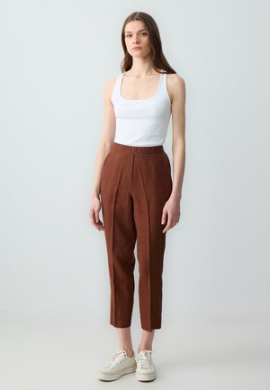 Koffiekleurige linnen broek met een hoge taille, plooien en zijzakken, gecombineerd met een witte geribde tanktop en witte sneakers.