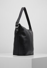 Svart axelväska i läder med strukturerad yta, rektangulär form, justerbar rem och cirkulär metallaccent.