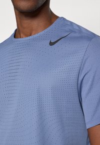 Maglietta Nike a maniche corte di colore azzurro chiaro, con un texture perforata traspirante. Presenta un logo Nike nero sulla spalla sinistra.