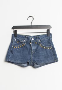 Shorts de mezclilla en color azul, con acentos de tachuelas doradas en los bolsillos frontales y costuras amarillas en contraste. Colgados de una percha negra.