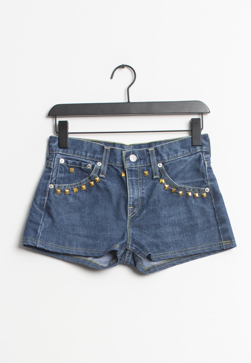Shorts de mezclilla en color azul, con acentos de tachuelas doradas en los bolsillos frontales y costuras amarillas en contraste. Colgados de una percha negra.